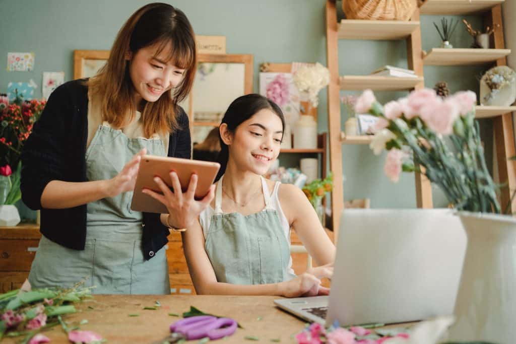 Happy multiracial women working on gadgets in floral store